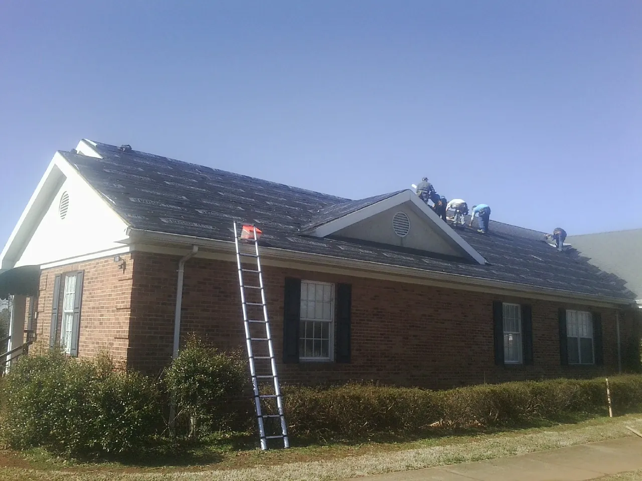 Crew tearing shingles off a brick ranch roof with a ladder set — Metal Roof Repair work by our crew in Moscow