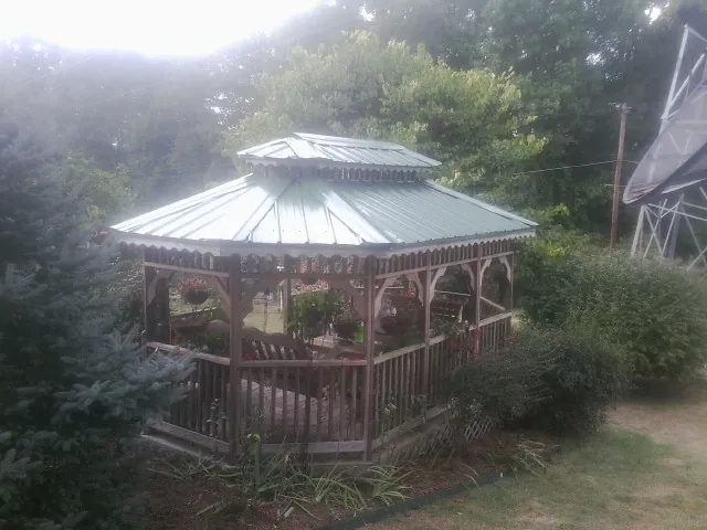 Green metal roof on a backyard gazebo surrounded by garden beds in Moscow